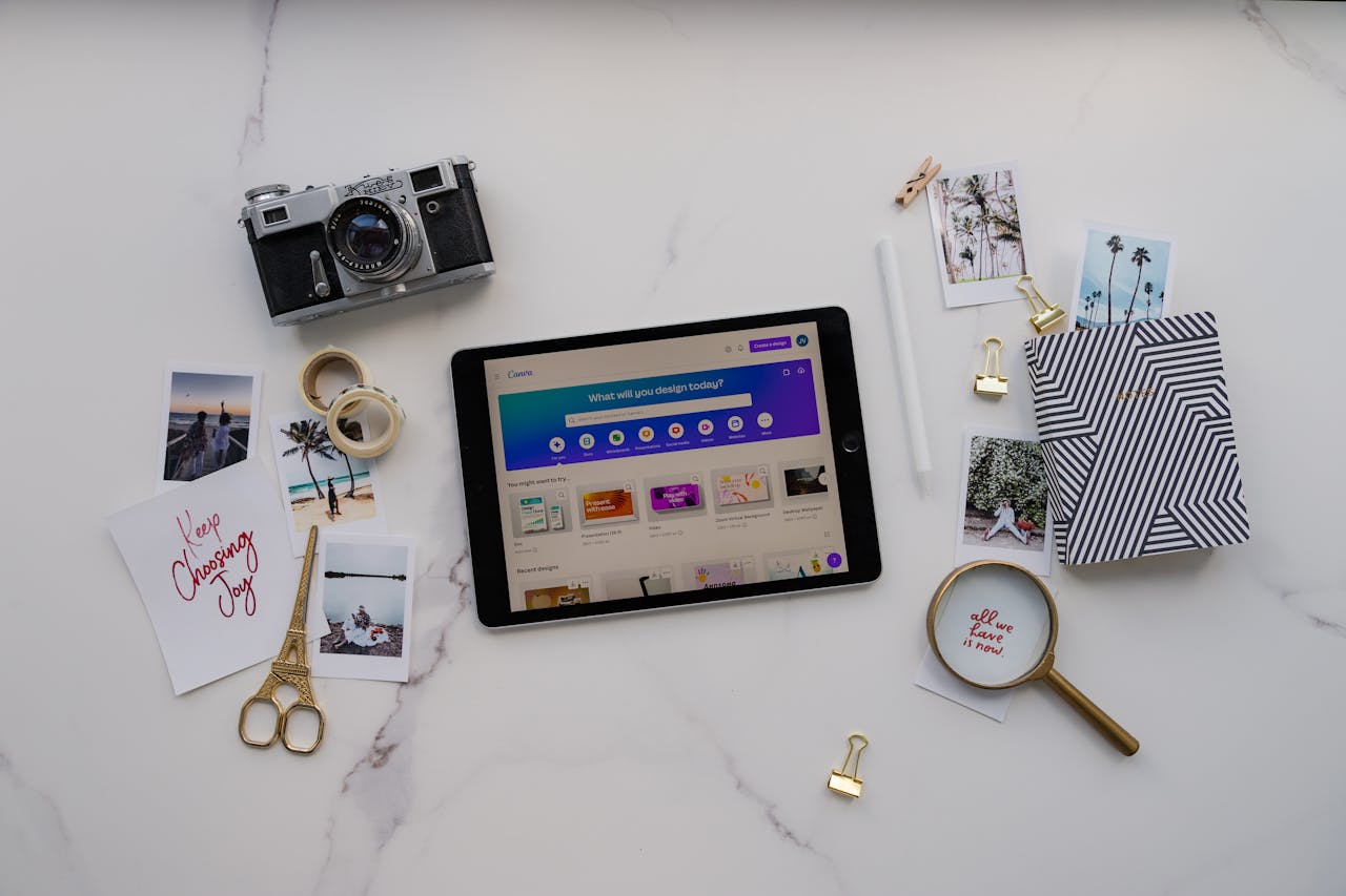 Modern creative workspace featuring a tablet, photos, and vintage camera on a marble background.